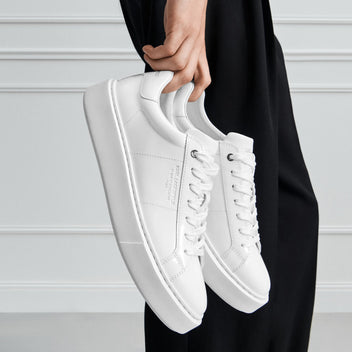 White sneakers held by a person against a neutral background